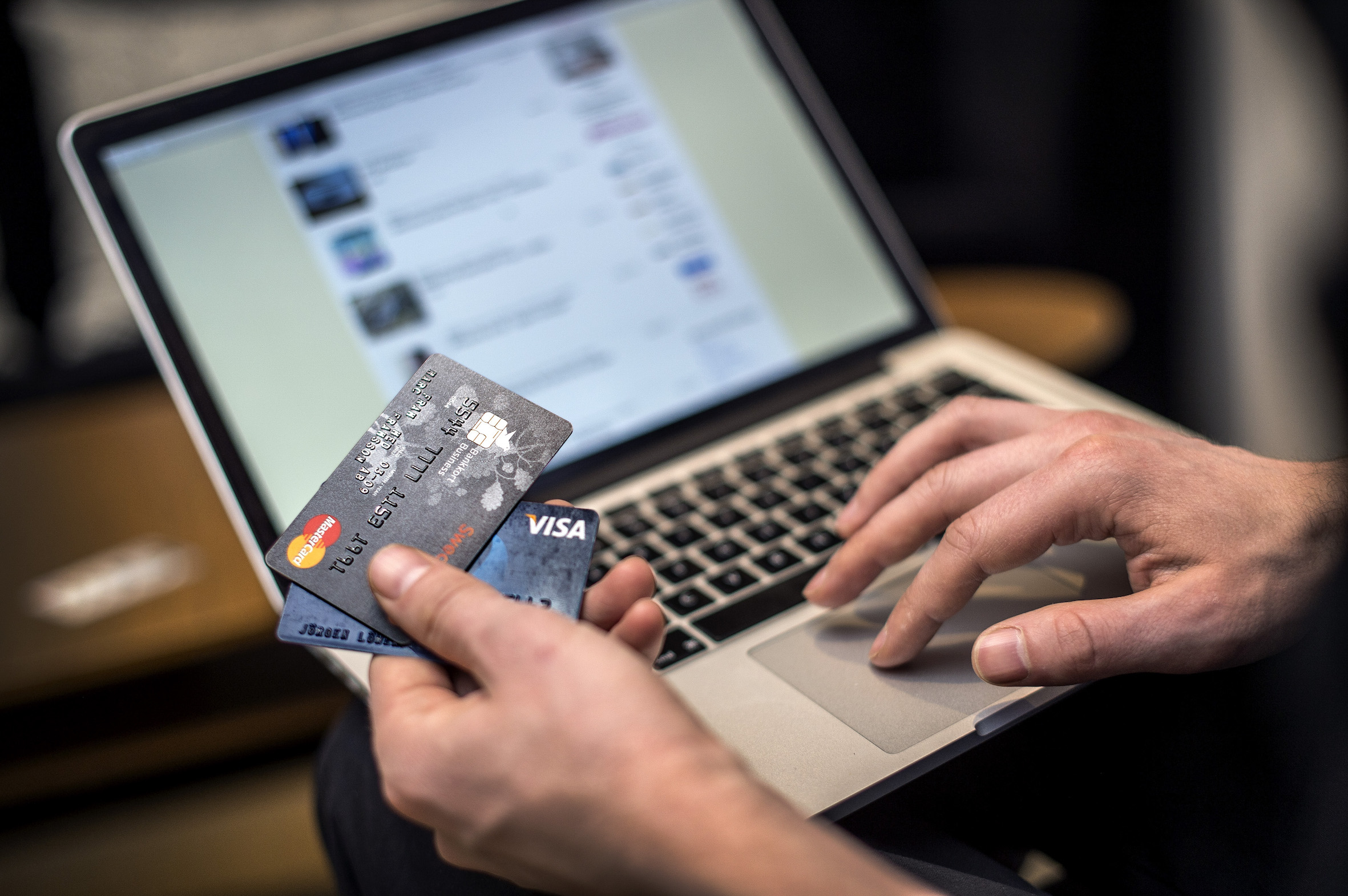 Person sitter vid datorn med kreditkort i handen